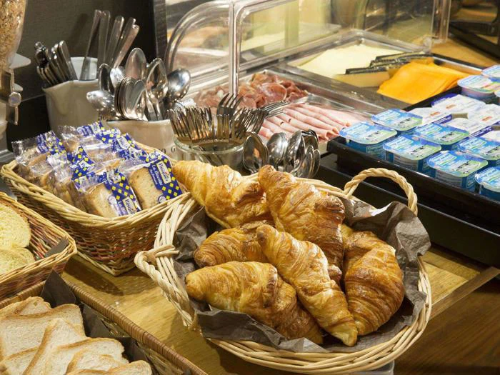 En morgenmadsbuffet med en kurv med croissanter, toastbrød, brødskiver, bestik, diverse pålæg, ost og individuelle smørportioner.