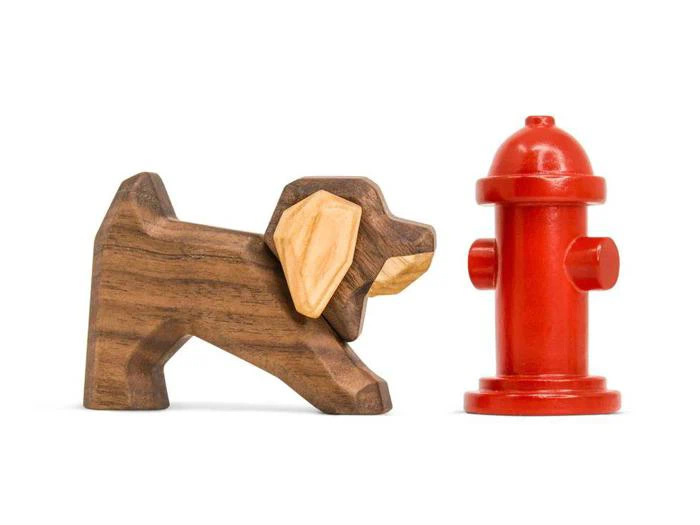 En træfigur af en hund med solbrune ører står ved siden af en lille rød brandhane på en hvid baggrund.