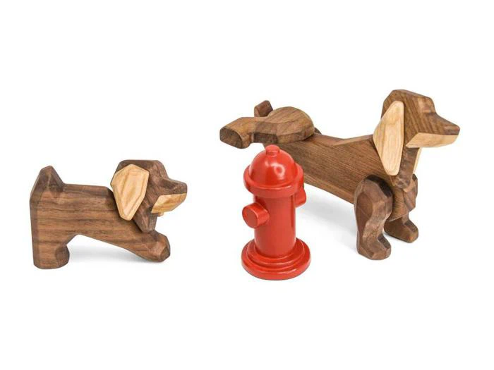 To hundefigurer af træ, en stor og en lille, er placeret i nærheden af en lille rød brandhane på en hvid baggrund.