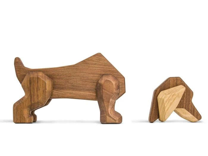 To hundefigurer af træ, den ene står oprejst og den anden ser ud til at snuse eller lege, begge udformet med enkle geometriske former.