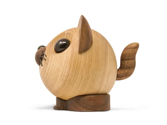 En kattefigur i træ med rund krop, opretstående hale og store sorte øjne, set fra siden på en hvid baggrund.