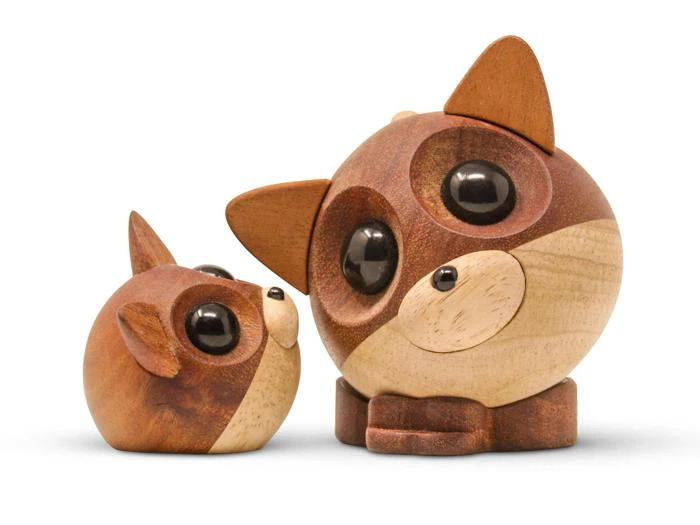 To runde vaskebjørnefigurer af træ med store sorte øjne, brun og beige farve og spidse ører, der sidder side om side på en hvid baggrund.