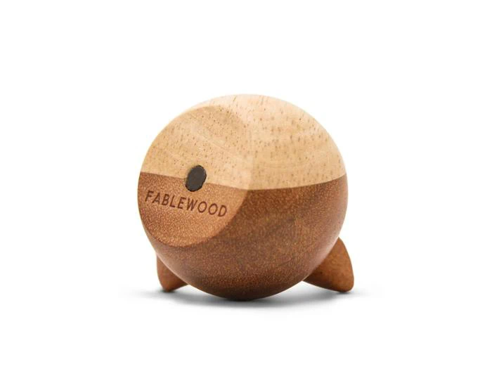 En rund, tofarvet træfigur med små ben, hvor ordet FABLEWOOD og en prik er indgraveret på den lysere overdel.