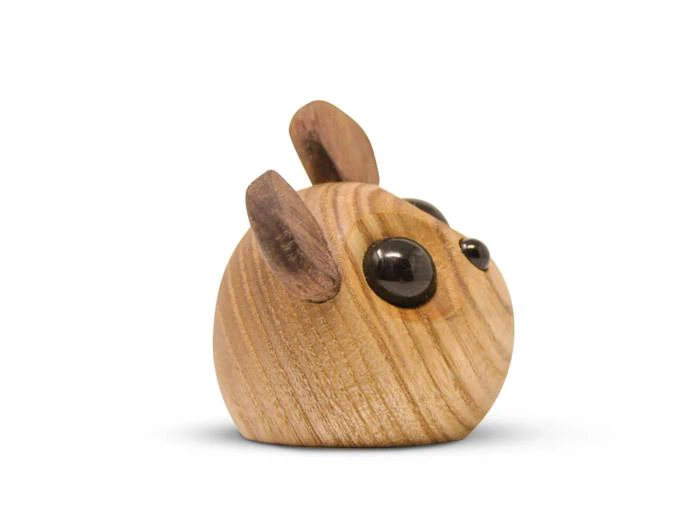 En lille, rund træfigur med store sorte øjne og to opretstående ører, der ligner et dyr, på en hvid baggrund.
