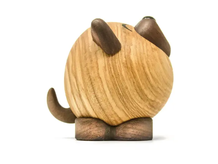 En rund træfigur, der ligner en hund med mørke ører, næse, fødder og hale, set bagfra på en hvid baggrund.