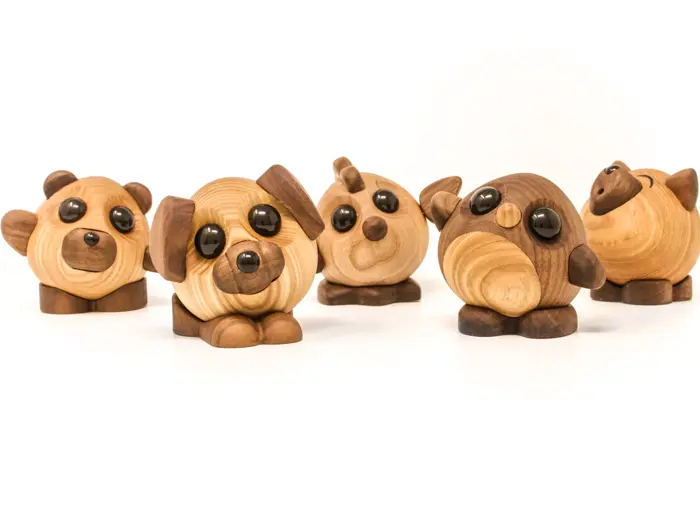 Fem små, runde dyrefigurer af træ med store, sorte øjne, bl.a. en hund, en bjørn, en fugl og en gris, på en hvid baggrund.