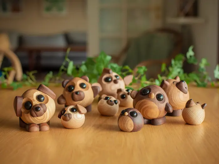 En gruppe søde, runde trædyrfigurer med store øjne er arrangeret på en træflade med grønne planter i baggrunden.