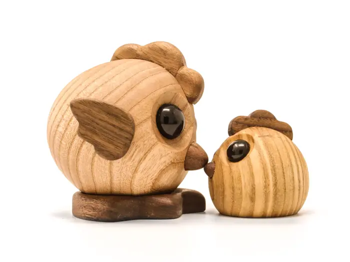 To uglefigurer af træ, en stor og en lille, står tæt over for hinanden, som om de rører ved hinanden med næbbet. Begge har runde, sorte øjne og er lavet af lyst og mørkt træ.