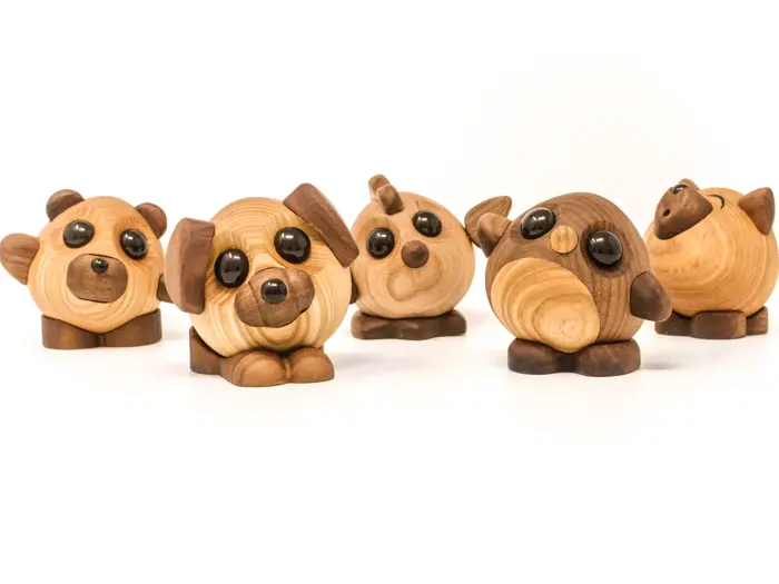 Fem søde dyrefigurer af træ med store runde øjne står på rad og række på en hvid baggrund.