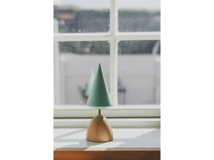 En lille træfigur med en grøn kogle på toppen, der ligner et minimalistisk træ, står i en vindueskarm, hvor sollyset strømmer ind.