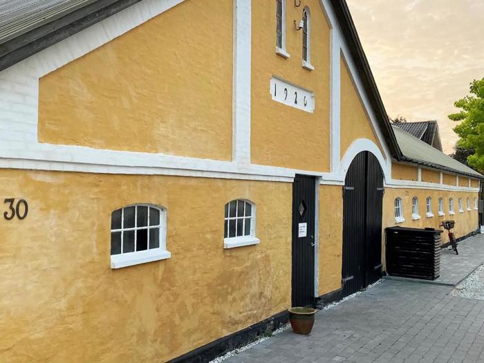 En lang gul bygning med hvid kant, sort buet dør og små vinduer. Nummeret 1924 står over døren, og nummer 30 står på venstre væg.