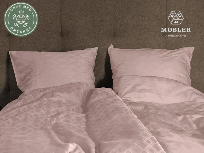 To pænt opredte enkeltsenge med lyserødt sengetøj og puder, placeret side om side mod et gråt, polstret hovedgærde. Logoer er synlige i de øverste hjørner.