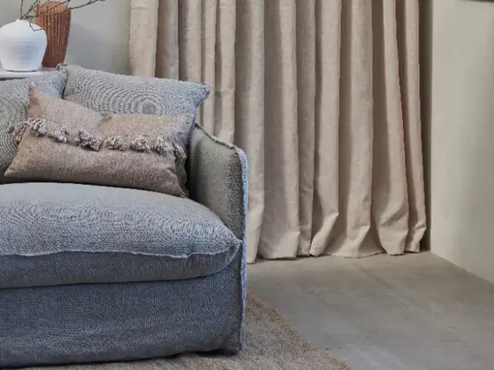 En blød grå lænestol med en struktureret pude og en pude med kvaster sidder ved siden af beige gardiner i et hyggeligt, moderne rum.