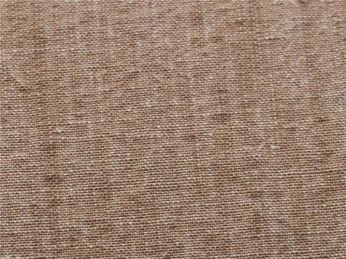 Nærbillede af lysebrunt vævet stof med en grov tekstur, synlige tråde og små pletter i hele overfladen.