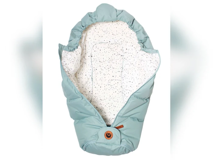 Lyseblå babykokon med hvidt, spættet inderfor. Kokonen har en top med hætte og en rund, brun knap nederst i midten.