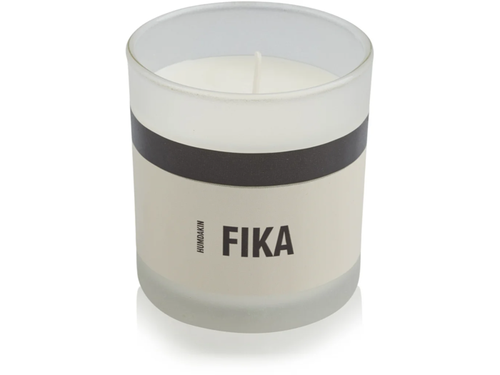 Et hvidt lys i en frostet glaskrukke med en sort stribe og ordet FIKA trykt på etiketten.