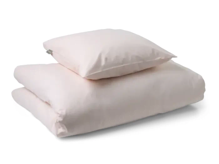 En foldet lyserød dyne med en matchende pude stablet ovenpå, begge med en blød, glat tekstur.