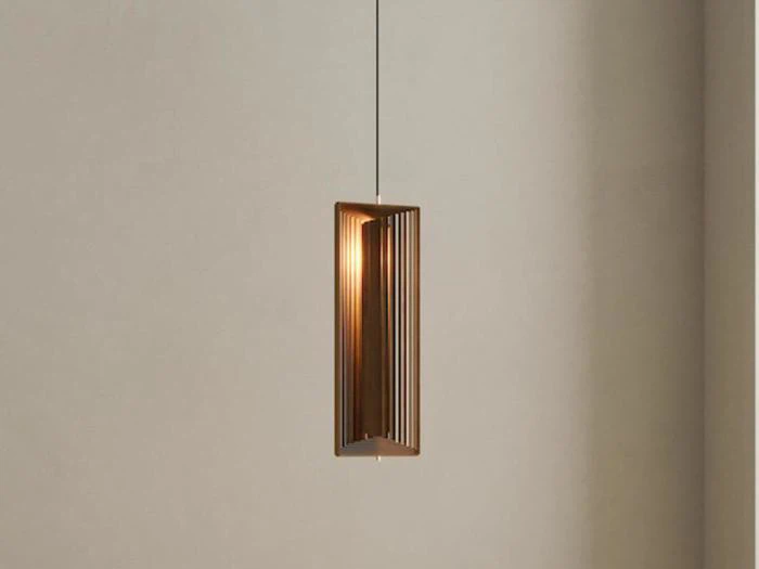Minimalistisk pendel med en rektangulær, lodret ramme af trælameller, ophængt fra loftet mod en almindelig beige væg.