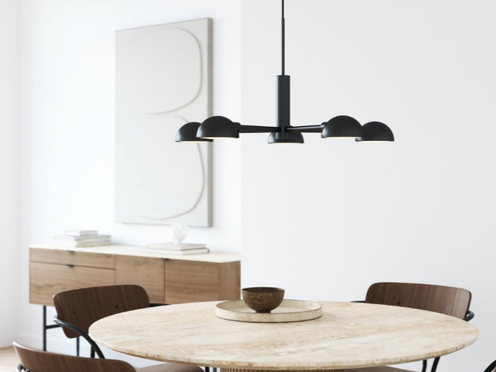 En moderne spiseplads med et rundt marmorbord, fire brune stole, en sort pendel, en træskænk og abstrakt vægkunst i et lyst, minimalistisk rum.