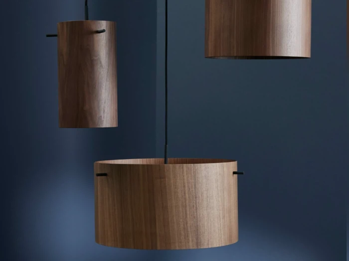 Tre cylindriske træpendler hænger på en mørkeblå baggrund, hver i forskellig størrelse og ophængt i sorte snore.