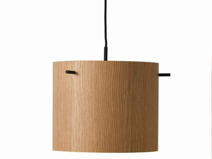 En cylindrisk pendel i træ med naturlig trækornfinish, der hænger i en sort ledning mod en almindelig hvid baggrund.