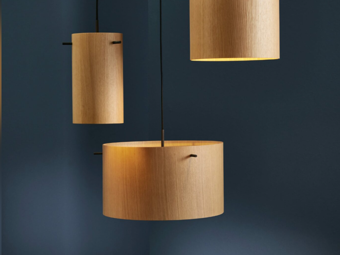 Tre cylindriske træpendler hænger op ad en mørkeblå væg med varmt lys, der stråler inde fra skærmene.