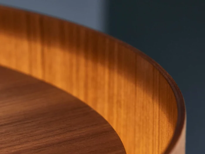 Nærbillede af en træoverflade med en buet kant med varmt lys og synlige træårer. Baggrunden er blødt sløret i blå og mørke toner.