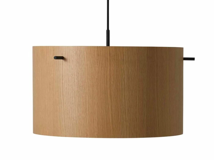 Minimalistisk cylindrisk pendellampe i træ med en glat, naturlig træfinish, ophængt i en sort ledning fra oven mod en hvid baggrund.