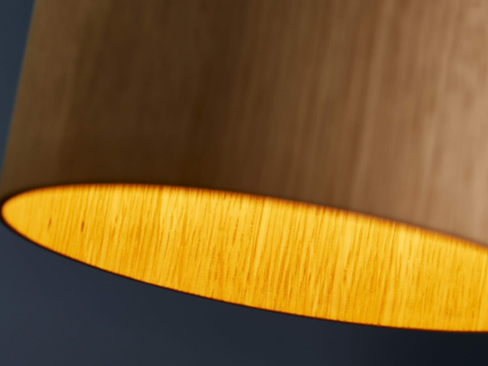 Nærbillede af en lampeskærm af træ med varmt lys, der gløder indeni og fremhæver træets struktur mod en mørk baggrund.