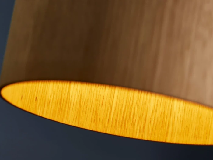 Nærbillede af en lampeskærm af træ med varmt lys, der gløder indeni og fremhæver træets struktur mod en mørk baggrund.