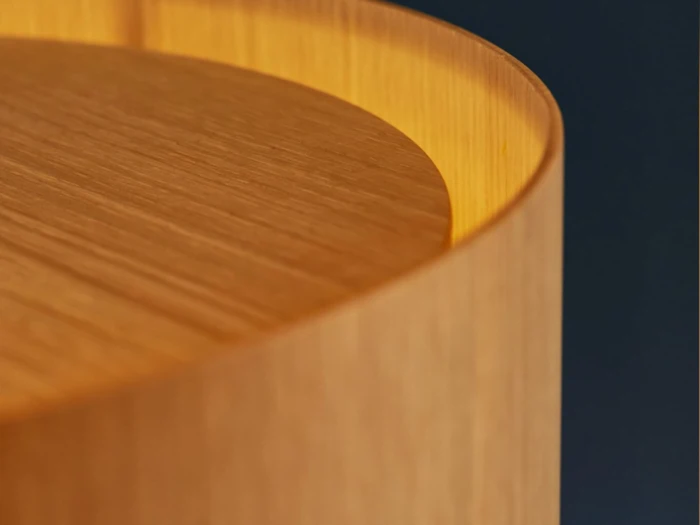 Nærbillede af en glat, buet træoverflade med varm belysning, der fremhæver træets årer og afrundede kanter mod en mørk baggrund.