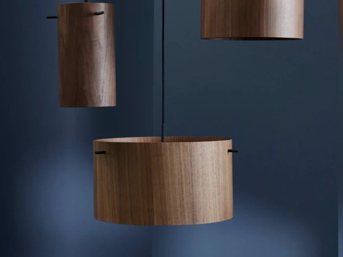 Tre cylindriske træpendler hænger på en mørkeblå baggrund, og hver skærm har en glat, naturlig trækornfinish.