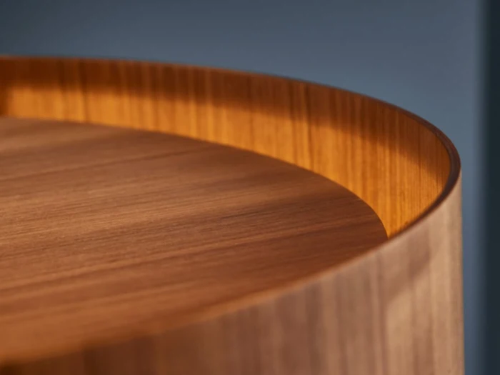 Nærbillede af en rund træbordplade med en buet, hævet kant, der viser de glatte træårer og varme brune toner.