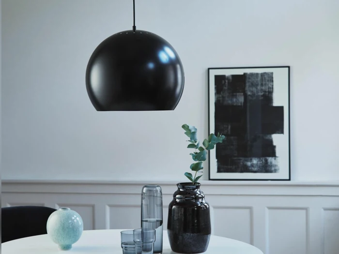 En moderne spiseplads med et rundt hvidt bord, sort pendellampe, sorte og blå vaser, glas og abstrakte sort-hvide kunstværker på væggen.