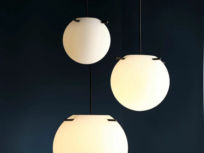 Tre moderne, sfæriske pendellamper med matte, hvide kugler hænger på en mørkeblå baggrund og skaber et minimalistisk og elegant udtryk.