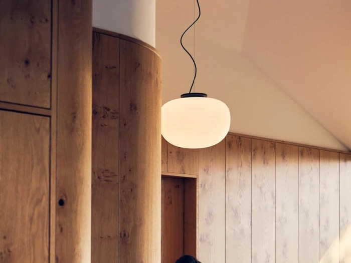 En rund, hvid pendel hænger fra loftet i et rum med lyse træpaneler på væggene og buede trædetaljer.