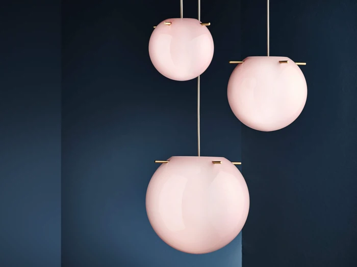 Tre moderne pendler med glatte, ovale skærme af frostet rosa glas hænger mod en mørkeblå væg.