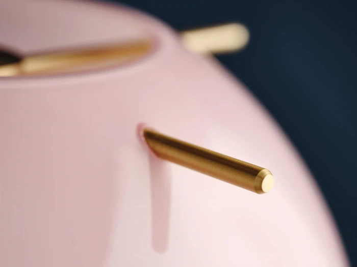 Nærbillede af et lyserødt, blankt objekt med cylindriske guldstænger, der stikker ud fra det, på en mørkeblå baggrund.