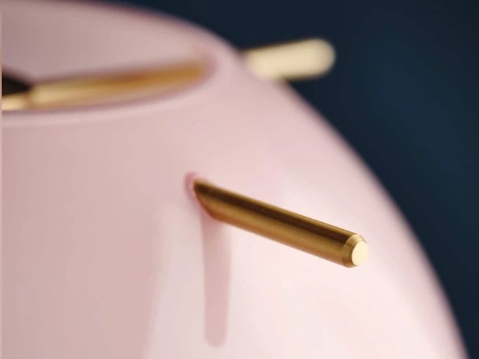 Nærbillede af en glat, blank lyserød overflade med gyldne stænger, der stikker ud fra den, mod en mørkeblå baggrund.