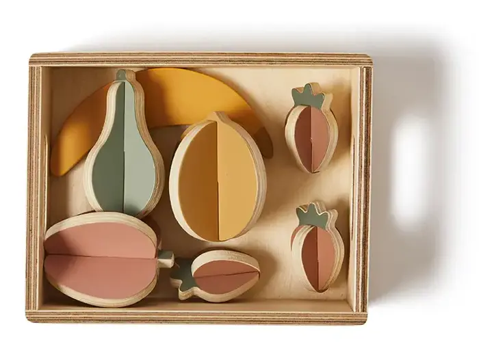 Legetøjsfrugtsæt af træ i en rektangulær æske med stykker formet som en banan, pære, appelsin, æble og to jordbær i dæmpede pastelfarver.