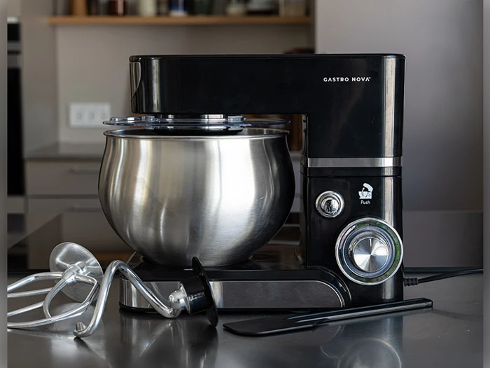 En sort Gastro Nova røremaskine med en stor skål i rustfrit stål står på køkkenbordet sammen med et piskeris, en dejkrog og en spatel.