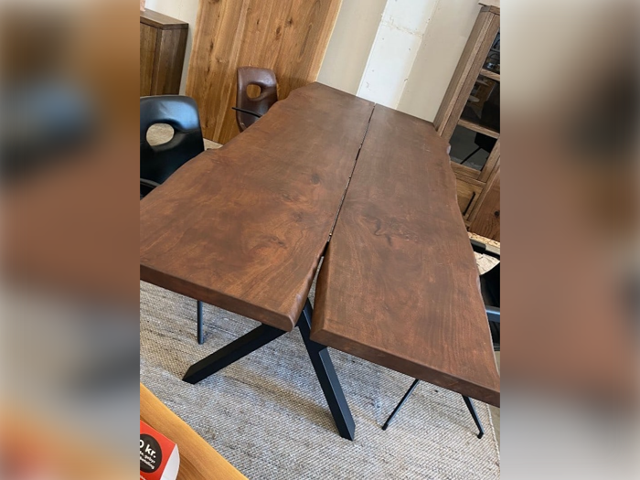 Et spisebord i træ med en naturlig deling på midten, sat på sorte metalben, omgivet af sorte stole i et moderne rum.