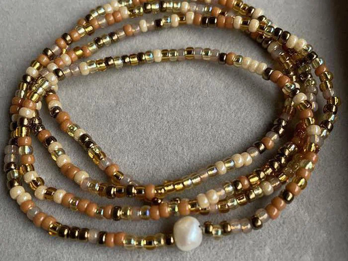 En perlekæde med små brune, gyldne og beige perler, der er viklet ind i sløjfer og har en enkelt hvid perlelignende perle.