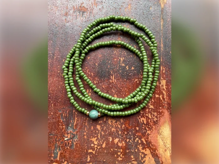En lang streng af små grønne perler med en større perle er rullet op på en rustik, rødbrun træoverflade.