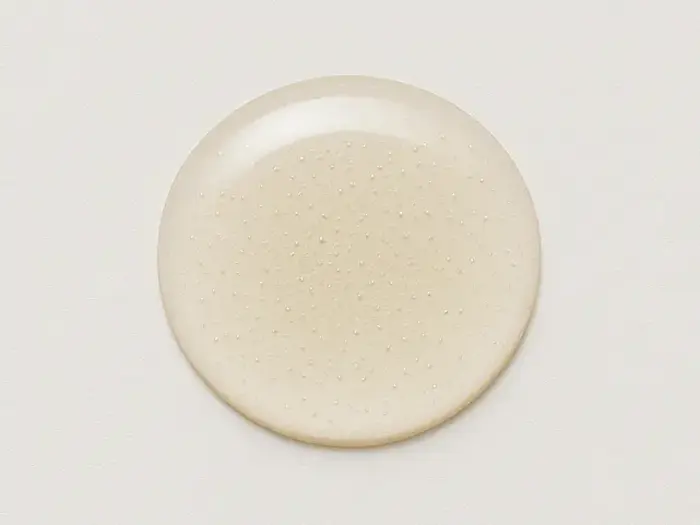 En rund, klar gellignende dråbe med små bobler indeni, placeret på en almindelig, lys overflade.