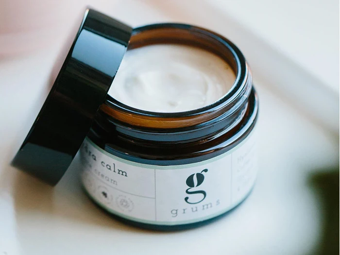 En åben krukke med Grums Hydra Calm ansigtscreme med låget vippet til siden, så man kan se det cremede produkt indeni.