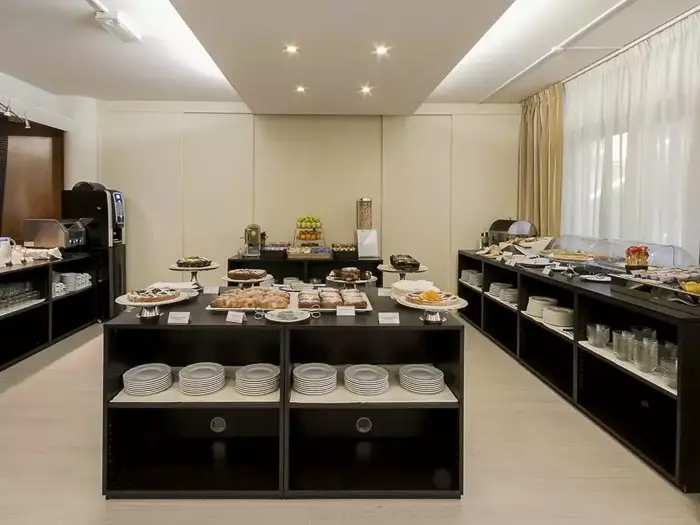 En veloplyst morgenbuffet med forskellige kager, frugter og retter på sorte borde, omgivet af hylder med tallerkener og glas.