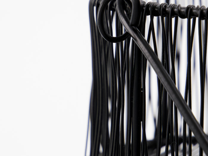 Nærbillede af sorte metaltråde, der danner et abstrakt geometrisk mønster mod en hvid baggrund.