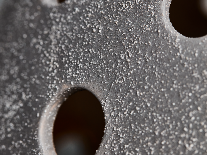 Nærbillede af en grå overflade med grov, kornet tekstur og flere cirkulære huller.