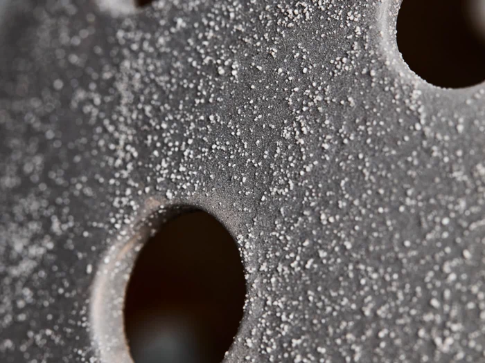 Nærbillede af en grå overflade med grov, kornet tekstur og flere cirkulære huller.